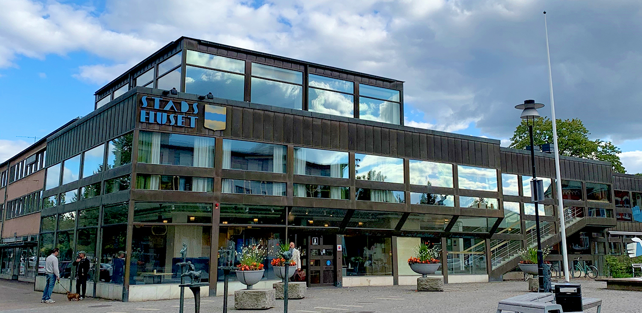Stadshuset i Värnamo. Det är en solig dag med blå himmel och några moln som speglar sig i Stadshusets fönster.