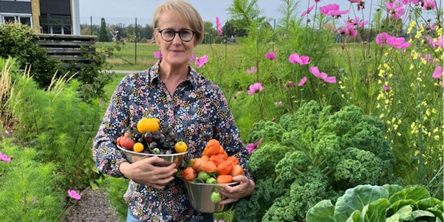 Kerstin Sneath, kvinna med glasögon, kort ljust hår och blommig skjorta. Håller i skålar med olika grönsaker.