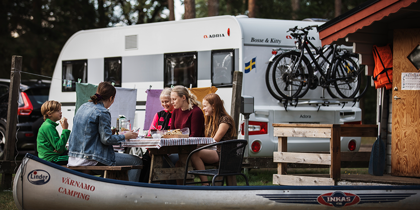 En familj som sitter och fikar på Värnamo camping. Bakom dem finns en husbil med cyklar och en kanot.
