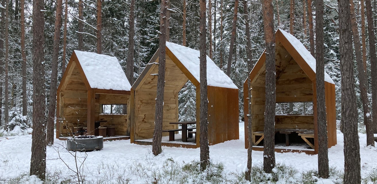 Tre vindskydd som ser ut som små hus står i vinterskrud och snö.