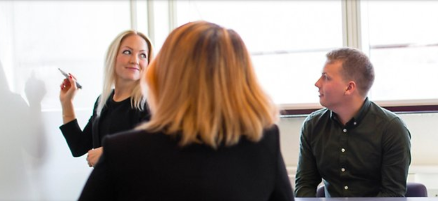 Kvinna skriver på väggtavlan och en grupp människor ser på.