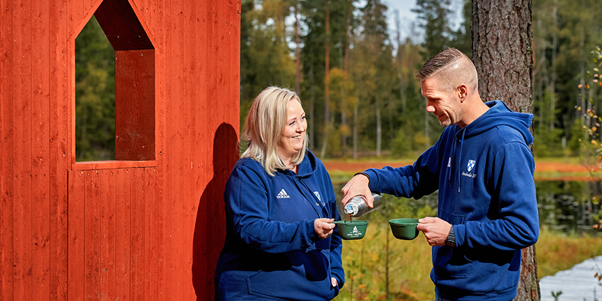 Två personer framför ett vindskydd. Mannen i bilden häller upp en kopp kaffe till kvinnan