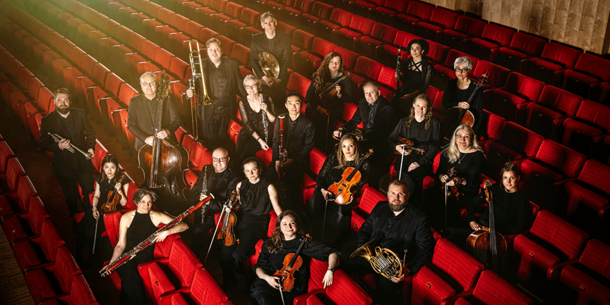 Musiker i Jönköpings sinfonietta sitter i röda konsertstolar med olika instrument i händerna.