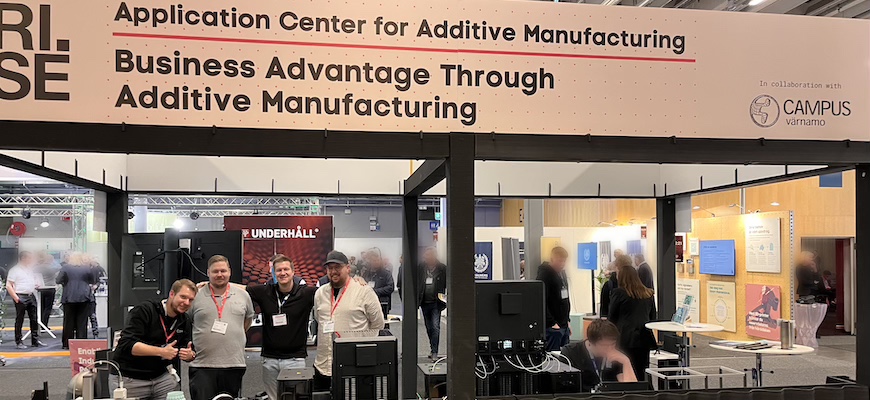 Bil på en monter under en 3d-printmässa. Fyra personer på bilden.