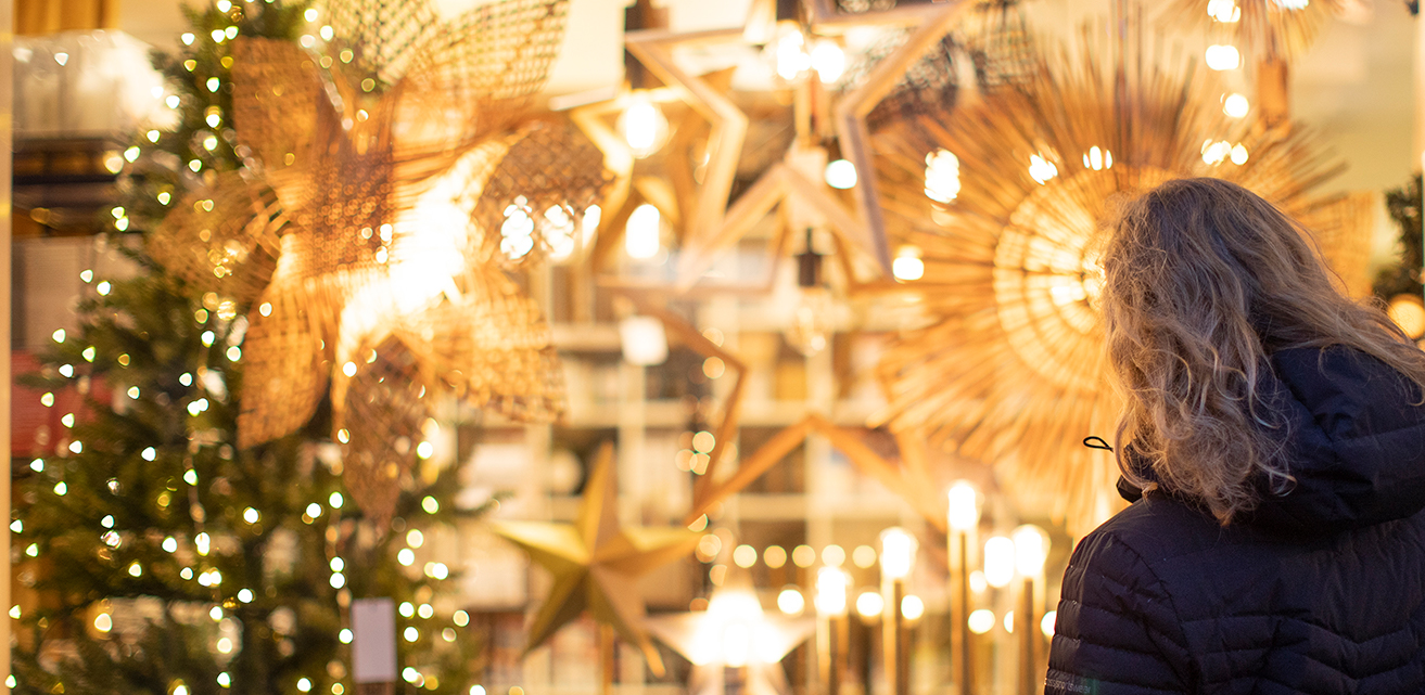 En kvinna står i en butik som lyser starkt av julstjärnor och lampor