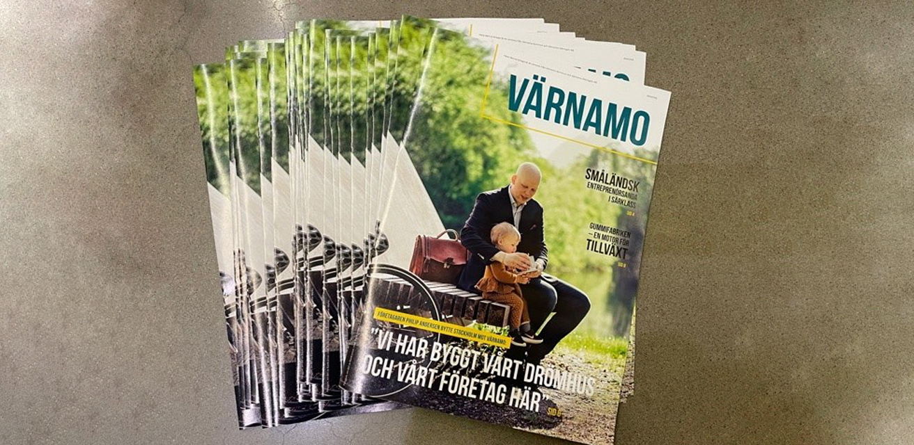 En hög av tidningar ligger på ett golv. Det är Värnamos bilaga från Dagens Industri, tryckt juni 2021. På framsidan sitter en man på bänken Polygon och visar en sak för sitt barn som sitter i mannens knä.