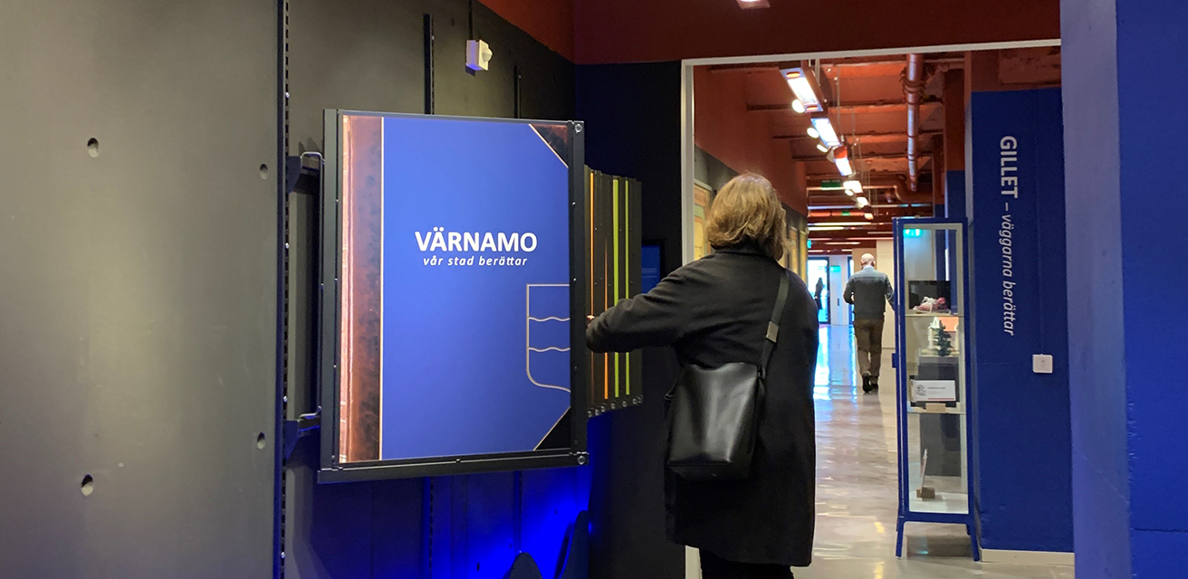 En kvinna bläddrar i väggboken som hänger i Gummifabriken på plan 0. Boken är blå, och på omslaget står: "Värnamo - vår stad berättar".