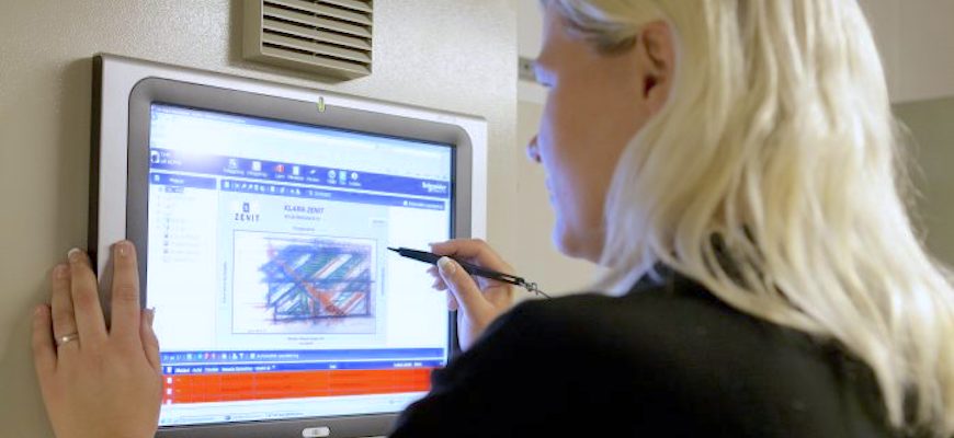 Kvinna står framför en vägghängd skärm och skriver på skärmen med en pekpenna.