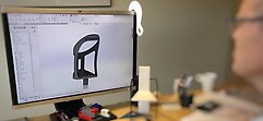 Foto på en datorskärm med med ett CAD-program som är öppet. En man som är suddig sitter och jobba med CAD-filen.