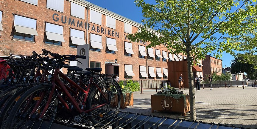 Cyklar som står på ett ställ. I bakgrunden syns Gummifabrikens entré.